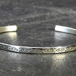 May include: A silver bangle bracelet with a geometric pattern etched into the surface.