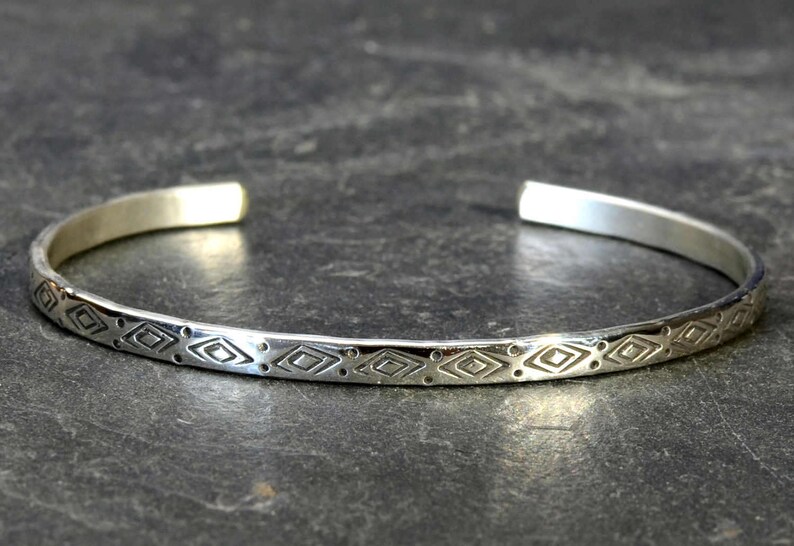 May include: A silver bangle bracelet with a geometric pattern etched into the surface.