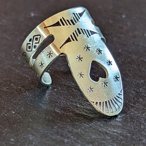 May include: Silver finger pick with a heart-shaped hole and a star pattern. The pick has a band that wraps around the finger.