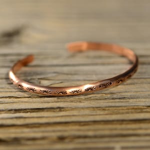 Pode incluir: Uma pulseira de cobre com acabamento martelado e um design de sol repetido.