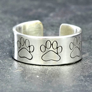 May include: A silver ring with three paw prints engraved on the band.