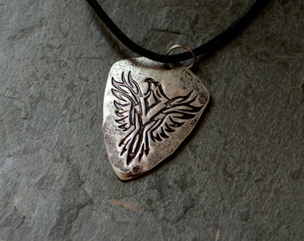 May include: A silver guitar pick necklace featuring a detailed etched design of a bird with outstretched wings.