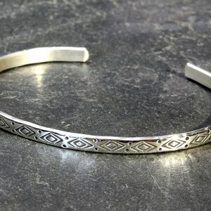 May include: A silver bangle bracelet with a geometric pattern etched into the surface.
