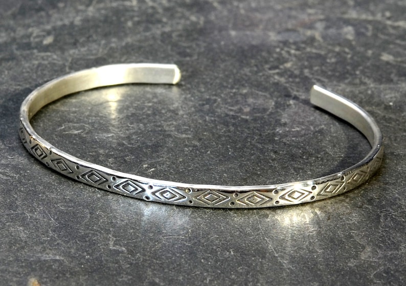May include: A silver bangle bracelet with a geometric pattern etched into the surface.