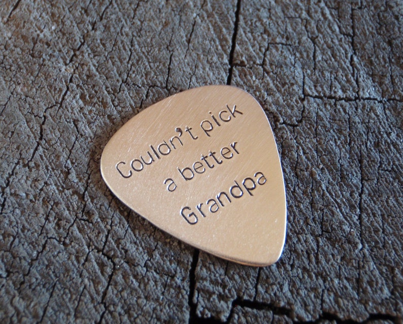 May include: Silver guitar pick with the text "Couldn't pick a better Grandpa" engraved on it.