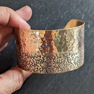 May include: A hammered brass cuff bracelet with a sunflower design. The bracelet is a wide cuff style and has a textured hammered finish.