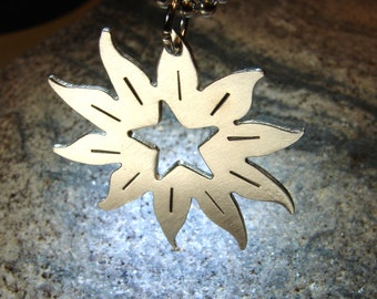 May include: A silver pendant in the shape of a starburst with a star cut out in the center. The pendant is hanging from a silver chain.