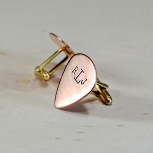 May include: A pair of gold cufflinks with a copper guitar pick shape. The pick has the initials "RLJ" engraved on it.