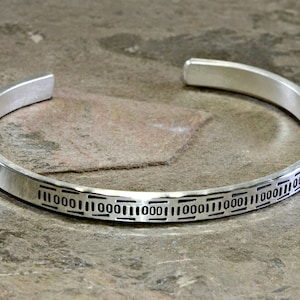 Può includere: Un braccialetto rigido in argento con un motivo geometrico inciso attorno alla fascia.