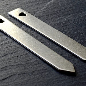 Puede incluir: Dos marcadores de plantas de metal plateado con un corte en forma de coraz&oacute;n. Los marcadores miden aproximadamente 12,5 cm de largo y tienen un extremo puntiagudo.