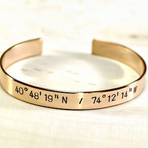 May include: A gold-toned metal bracelet with the coordinates "40° 48' 19" N / 74° 12' 14" W" engraved on it.