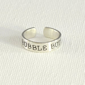 May include: A silver toe ring with the words "Bubble Butt" engraved on it.