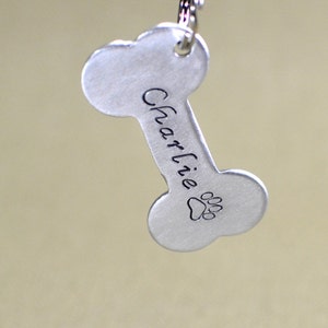 May include: Silver bone-shaped dog tag with the name "Charlie" engraved on it. A paw print is engraved below the name.