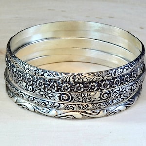 5 silver bangles with intricate floral designs. The bangles are stacked on top of each other, creating a layered look.