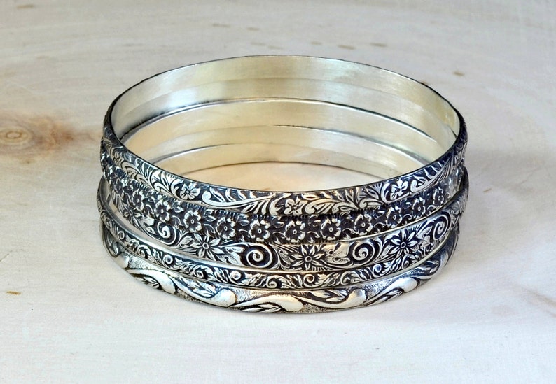 5 silver bangles with intricate floral designs. The bangles are stacked on top of each other, creating a layered look.
