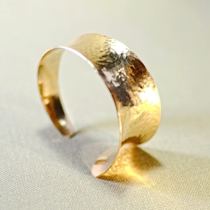 May include: A gold hammered cuff bracelet with a wide, curved band.