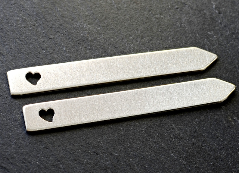 Puede incluir: Dos soportes de cuello de metal plateado con un corte en forma de coraz&oacute;n. Los soportes de cuello miden aproximadamente 5 cm de largo.