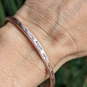 May include: A silver bangle bracelet with a repeating sun design engraved around the band.