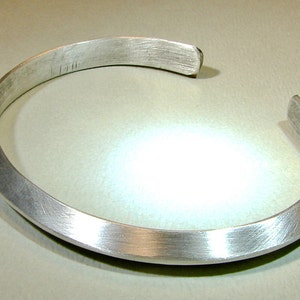 May include: A silver bracelet with a brushed finish. The bracelet is open and has a slightly curved shape.