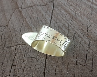 May include: Silver guitar pick with a personalised inscription that reads "Andy Roswell" and a small guitar symbol.