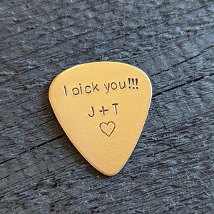 May include: A gold-colored guitar pick with the text "I pick you!!!" and "J+T" with a heart symbol.