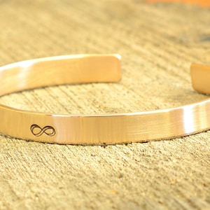 May include: A gold-toned infinity symbol engraved on a brushed metal bangle bracelet.