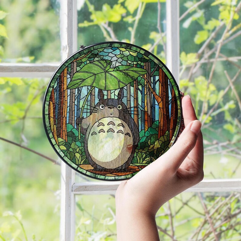 May include: A round stained glass panel featuring a cartoon character in a forest scene. The character is gray with a white belly and holds a large green leaf. The background includes trees and a blue sky, with a black border.