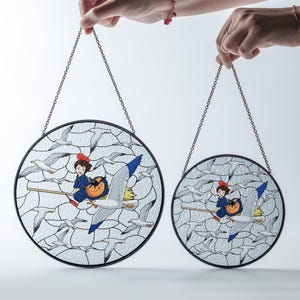 May include: Two round stained glass panels with a black border and chain for hanging. Each panel features a cartoon girl on a broom riding a seagull, surrounded by other seagulls. The girl wears a blue dress and red bow.