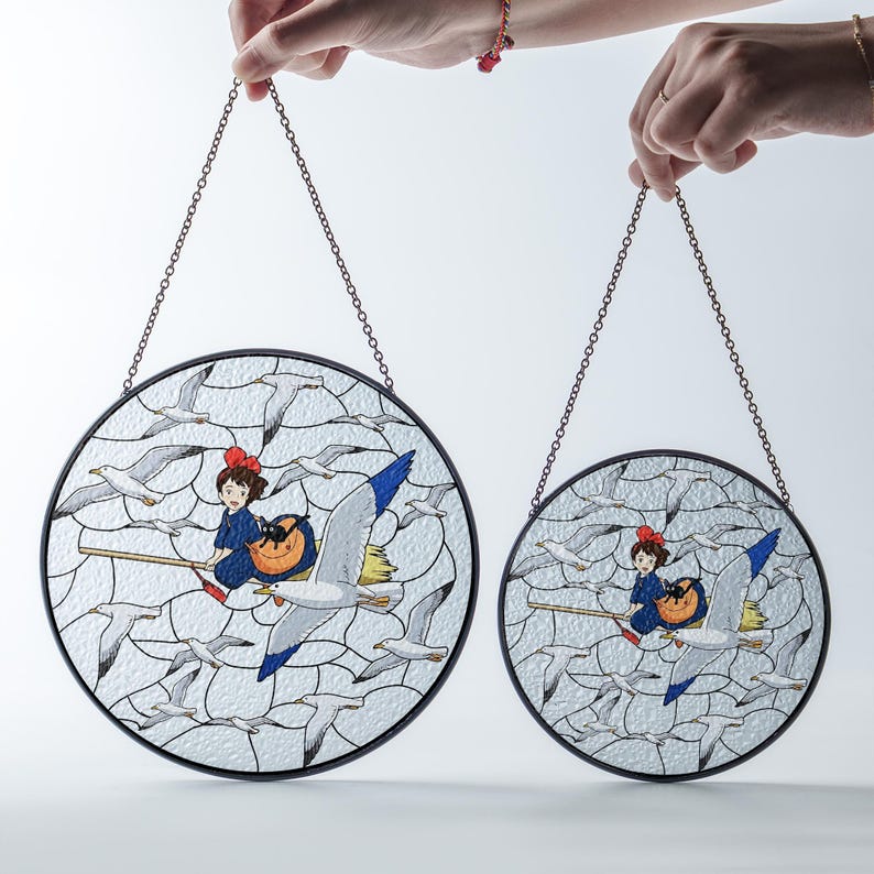 May include: Two round stained glass panels with a black border and chain for hanging. Each panel features a cartoon girl on a broom riding a seagull, surrounded by other seagulls. The girl wears a blue dress and red bow.