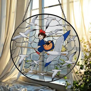 May include: Round stained glass window art featuring a young girl on a broom with a black cat, surrounded by seagulls. The girl wears a blue dress and a red bow. The seagulls are white with gray and blue accents.