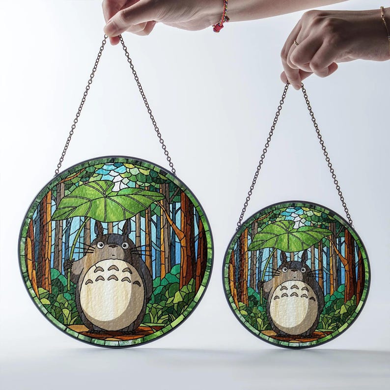May include: Two round stained glass panels featuring a forest scene with a cartoon character under a leaf umbrella. The panels are held by a chain and have a black border. The character is gray with a white belly.