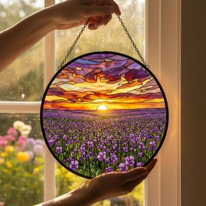 May include: Round stained glass panel depicting a sunset over a field of purple flowers. The sky transitions from orange to purple, with a bright yellow sun. The panel is held by a chain.