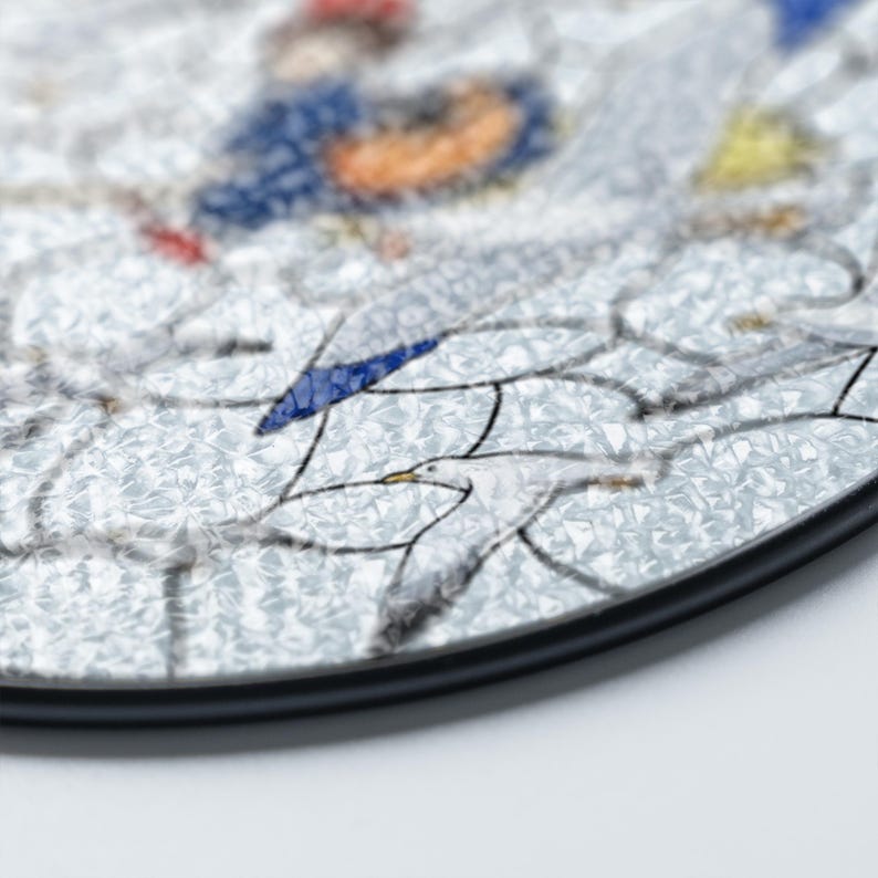 May include: Round decorative coaster with a detailed illustration of seagulls in flight. The coaster features a textured, light gray background with a black border. The artwork includes blue, yellow, and red accents.