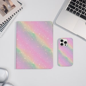 Könnte beinhalten: Eine pastellfarbene Tablet-Hülle und Handyhülle mit Regenbogen-Design. Die Hüllen haben ein rosa, lila und grünes Aquarellmuster mit weißen Sprenkeln. Die Handyhülle hat einen Kameraausschnitt.