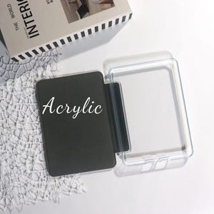 K&ouml;nnte beinhalten: Eine schwarze Acrylh&uuml;lle mit dem Wort "Acrylic" in wei&szlig;er Schrift. Die H&uuml;lle ist ge&ouml;ffnet und zeigt eine transparente Kunststoffschutzh&uuml;lle. Die Artikel befinden sich auf einer wei&szlig;en Oberfl&auml;che mit einem dekorativen Spitzemuster.