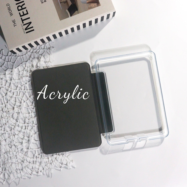 K&ouml;nnte beinhalten: Eine schwarze Acrylh&uuml;lle mit dem Wort "Acrylic" in wei&szlig;er Schrift. Die H&uuml;lle ist ge&ouml;ffnet und zeigt eine transparente Kunststoffschutzh&uuml;lle. Die Artikel befinden sich auf einer wei&szlig;en Oberfl&auml;che mit einem dekorativen Spitzemuster.