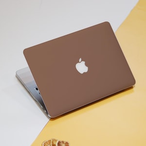 May include: A closed brown laptop computer with a white Apple logo on the lid. The laptop is sitting on a yellow surface.