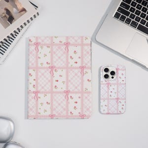 May include: A pink and white patterned tablet case and phone case. The cases feature a grid design with pink ribbons and small floral accents. The tablet case is rectangular, and the phone case is a rectangle with a camera cutout.