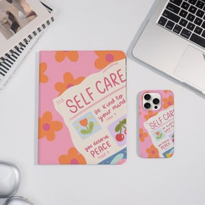 Puede incluir: Un cuaderno y una funda de teléfono rosas con un estampado floral y las palabras "SELF CARE" en fuente manuscrita. El cuaderno y la funda del teléfono también presentan las frases "Be kind to your mind" y "You deserve peace".