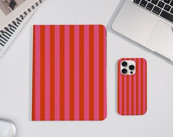 May include: A red and pink striped phone case and a matching notebook are displayed on a white surface. The phone case is next to a laptop and a closed notebook. The notebook and phone case have a vertical stripe pattern.