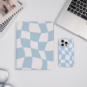 May include: A tablet case and a phone case feature a light blue and white wavy checkered design. A laptop and a book are also visible. The tablet case is rectangular, and the phone case has a camera cutout.