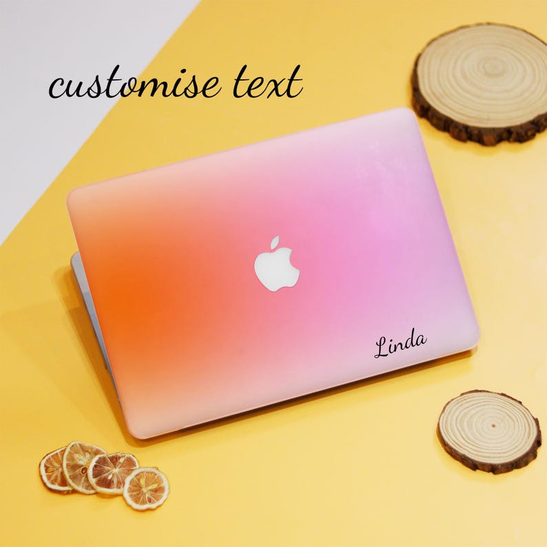 Puede incluir: Una piel de port&aacute;til rosa y naranja con un logotipo de Apple blanco y la palabra "Linda" impresa en ella. La piel est&aacute; sobre una superficie amarilla.