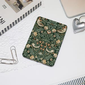 May include: A green and white patterned e-reader case with a floral design and small birds. The case has a dark green background with white flowers and leaves, and small orange birds with black eyes.