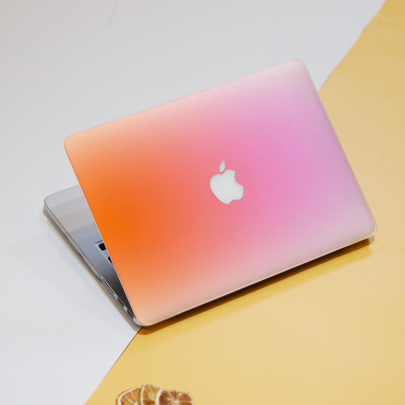 Puede incluir: Un ordenador port&aacute;til cerrado con un dise&ntilde;o degradado rosa y naranja en la tapa. El logotipo de Apple es visible en la tapa.