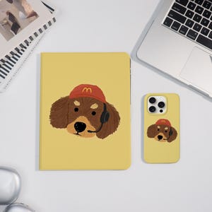 Könnte beinhalten: Gelbe Tablet- und Handyhülle mit einem Cartoon-Dackel, der einen roten Hut mit goldenem Bogenlogo und Headset trägt. Die Hüllen haben ein passendes Design und befinden sich auf einer weißen Oberfläche.