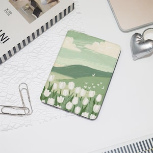 Può includere: Un tappetino per mouse rettangolare verde e bianco con un dipinto di paesaggio di dolci colline, tulipani bianchi e un cielo nuvoloso. Il tappetino è circondato da forniture per ufficio, tra cui un fermacarte a forma di cuore argentato e un laptop.