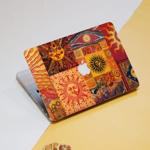 May include: A laptop computer with a colorful sticker featuring a patchwork design of suns with faces. The sticker has a red, orange, yellow, and blue color scheme.