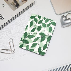 Puede incluir: Una funda de teléfono con estampado verde y blanco con un diseño de acuarela de hojas y flores.