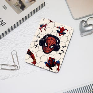 May include: A rectangular mousepad featuring a Spider-Man design. The design includes Spider-Man's mask with headphones, surrounded by lightning bolts and Spider-Man in various poses, set against a honeycomb pattern.