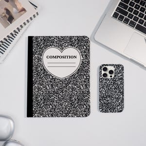 Könnte beinhalten: Ein Notizbuch und eine Smartphone-Hülle mit einem schwarz-weißen, gesprenkelten Design. Das Notizbuch hat ein herzförmiges Etikett mit dem Wort "COMPOSITION" in Schwarz aufgedruckt. Die Handyhülle hat ein passendes gesprenkeltes Muster.